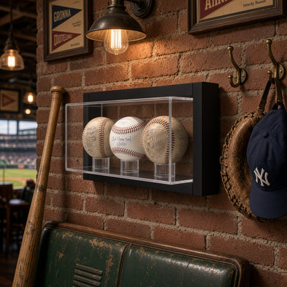 Framed 3 baseball case on a brick wall above a leather couch with a bat and cap nearby